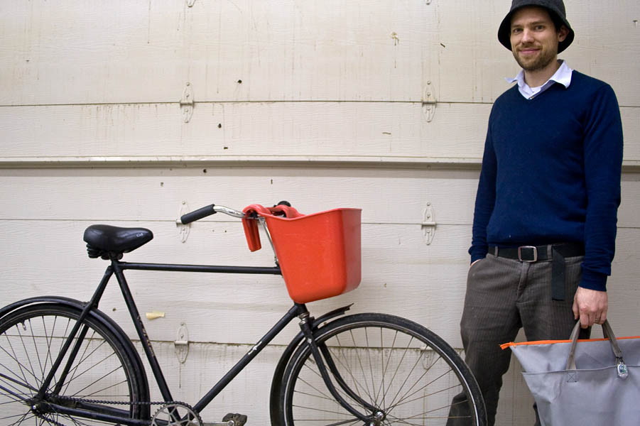 John stands with his Dutch bicycle and self-designed bike bucket and bag. The bucket was a purchase from a farm store and the bag was something he designed and sewed himself. John likes to see the bag as an extension of his desire to solve problems elegantly and simply.